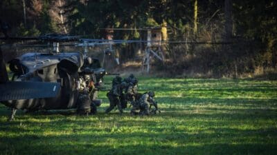 Soldaten in Tarnuniform steigen aus einem schwarzen Hubschrauber auf einer Wiese aus.