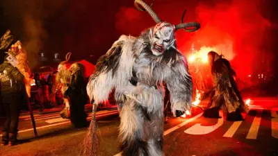 Krampusfigur mit gehörntem Gesicht und zotteligem Fell vor roter Beleuchtung