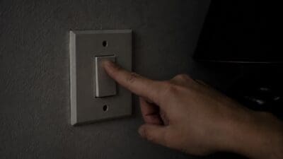 Eine Hand drückt mit dem Zeigefinger einen Lichtschalter an der Wand im Halbdunkel.