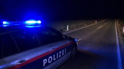 Polizeiwagen mit Blaulicht parkt am Rand einer dunklen Landstraße bei Nacht