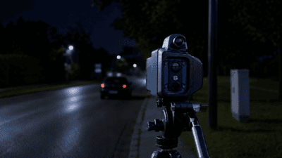 Eine Radarkamera auf einem Stativ steht an einer nassen Straße bei Nacht.