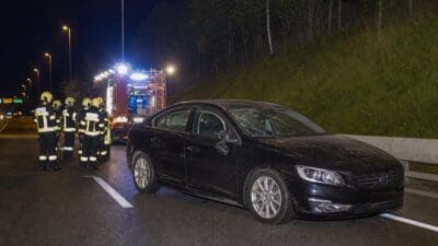 Feuerwehrleute in Schutzkleidung stehen neben einem beschädigten schwarzen Auto auf der Autobahn bei Nacht