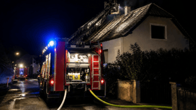 Feuerwehrfahrzeug mit ausgefahrener Drehleiter an einem Wohnhaus bei Nacht