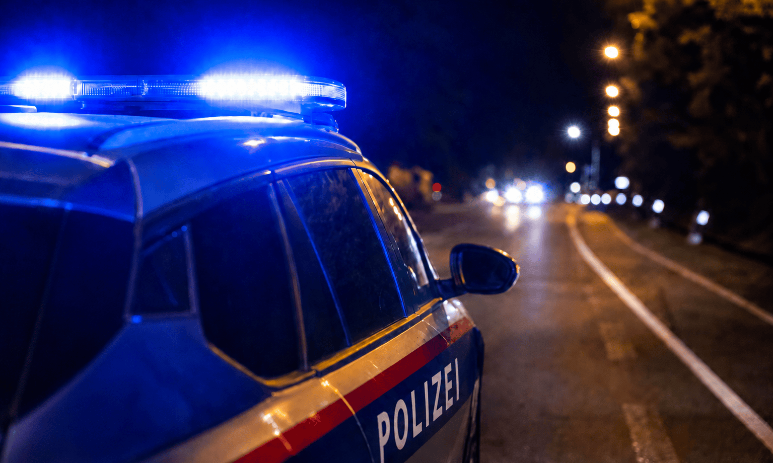 Seitenansicht eines Polizeifahrzeugs mit leuchtendem Blaulicht auf dem Dach bei Nacht