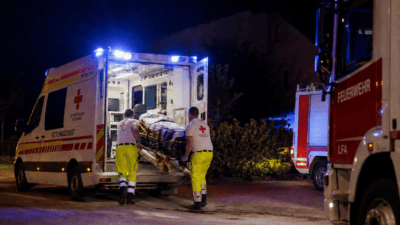 Zwei Sanitäter laden einen Patienten auf einer Trage in einen Rettungswagen bei Nacht.