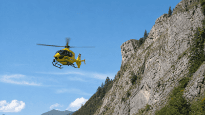 Gelber ÖAMTC-Rettungshubschrauber fliegt vor einer steilen Felswand in den Alpen