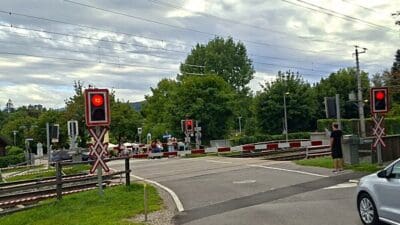 Rote Signallichter an einer Eisenbahnkreuzung mit Schranken und wartender Person in Krumpendorf