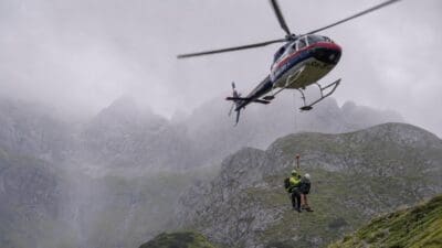 Polizeihubschrauber schwebt über einem nebligen Berggipfel mit zwei Personen auf einem Felsvorsprung.