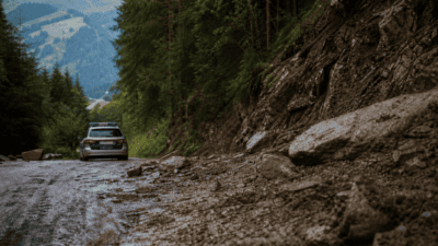 Polizeiauto steht auf nasser Bergstraße mit Schlamm Steinen und Geröll am Rand