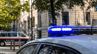 Blaues Blaulicht leuchtet auf dem Dach eines Polizeifahrzeugs in einer Wiener Stadtstraße.