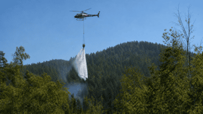 Polizeihubschrauber lässt einen Wasserstrahl über einem bewaldeten Berg herabregnen