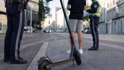 Polizisten kontrollieren einen Mann neben einem E-Scooter auf einer Straße in Wien.