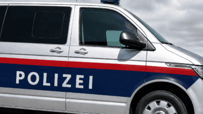 Seitenansicht eines silbernen Polizeivans mit POLIZEI-Aufschrift und blauer Warnleuchte unter grauem Himmel