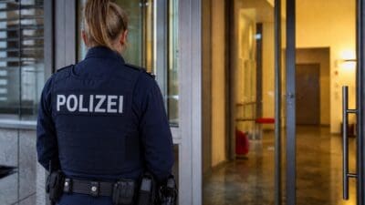 Rückenansicht einer Polizistin in Uniform vor einem modernen Gebäudeeingang mit Glasfassade