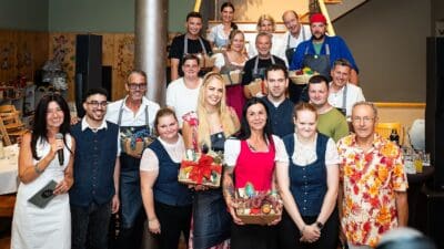 Gruppe von Erwachsenen in Schürzen und Freizeitkleidung mit Geschenkkörben vor einer Treppe