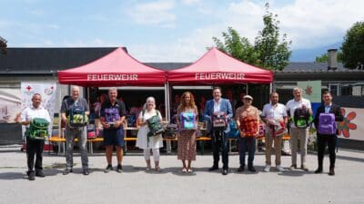 Gruppe von Menschen hält bunte Schultaschen vor roten Feuerwehrzelten in Reichenau