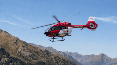 Roter und weißer Rettungshubschrauber der ARA Flugrettung fliegt über felsige Alpenberge.