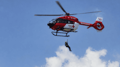 Rot-weißer Rettungshubschrauber der ARA Flugrettung mit einem Retter an einem Seil über Wolken