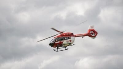 Roter und weißer Notarzt-Hubschrauber mit rotem Kreuz fliegt vor bewölktem Himmel
