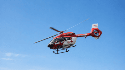 Roter und weißer Rettungshubschrauber mit rotem Kreuz fliegt vor blauem Himmel