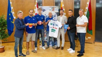 Gruppe von Männern bei der Pressekonferenz des SC Ferlach mit Handballtrikot und Fahnen.