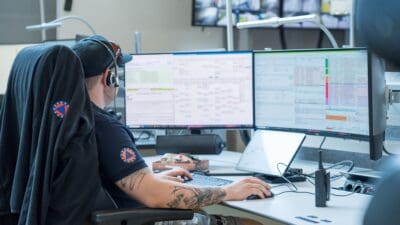 Mitarbeiter mit Headset und Cap sitzt vor mehreren Bildschirmen in einer Leitstelle.