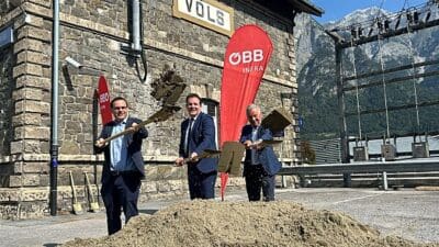 Drei Männer in Anzügen werfen Erde mit Schaufeln beim Spatenstich vor dem Bahnhof Völs.