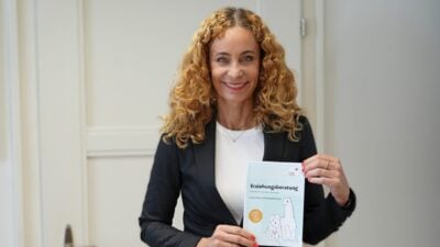 Eine lächelnde Frau mit blonden Locken hält eine Broschüre zur Erziehungsberatung.