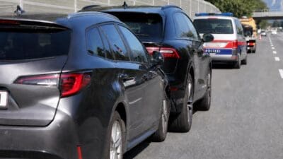 Reihe von schwarzen SUVs und einem Polizeifahrzeug auf der Autobahn mit Bergen im Hintergrund