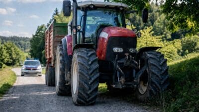 Roter Traktor mit Anhänger und Polizeiauto auf einem ländlichen Landweg.