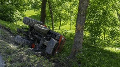 Umgekippter roter Mini-Traktor liegt neben einem Baum am Waldrand