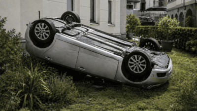 Silberner Pkw liegt auf dem Dach im Gras eines Innenhofs vor einem Gebäude