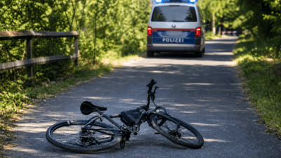 Ein umgestürztes Fahrrad liegt auf einem asphaltierten Weg vor einem Polizeiwagen mit Blaulicht.