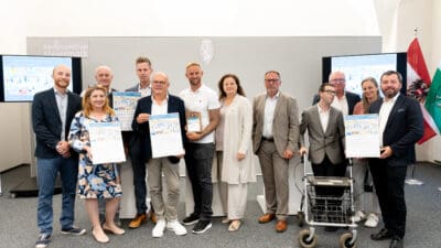 Zehn Personen stehen vor Bildschirmen mit VCÖ-Mobilitätspreis und halten Urkunden in den Händen