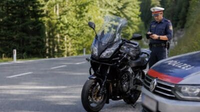 Polizist in Uniform steht neben einem Motorrad und einem Polizeiauto auf einer Waldstraße