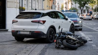 Weißes SUV und umgestürztes Motorrad auf einer Straße mit Polizeiwagen im Hintergrund