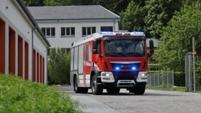 Rotes Feuerwehrfahrzeug mit leuchtenden blauen Blaulichtern vor einem weißen Gebäude