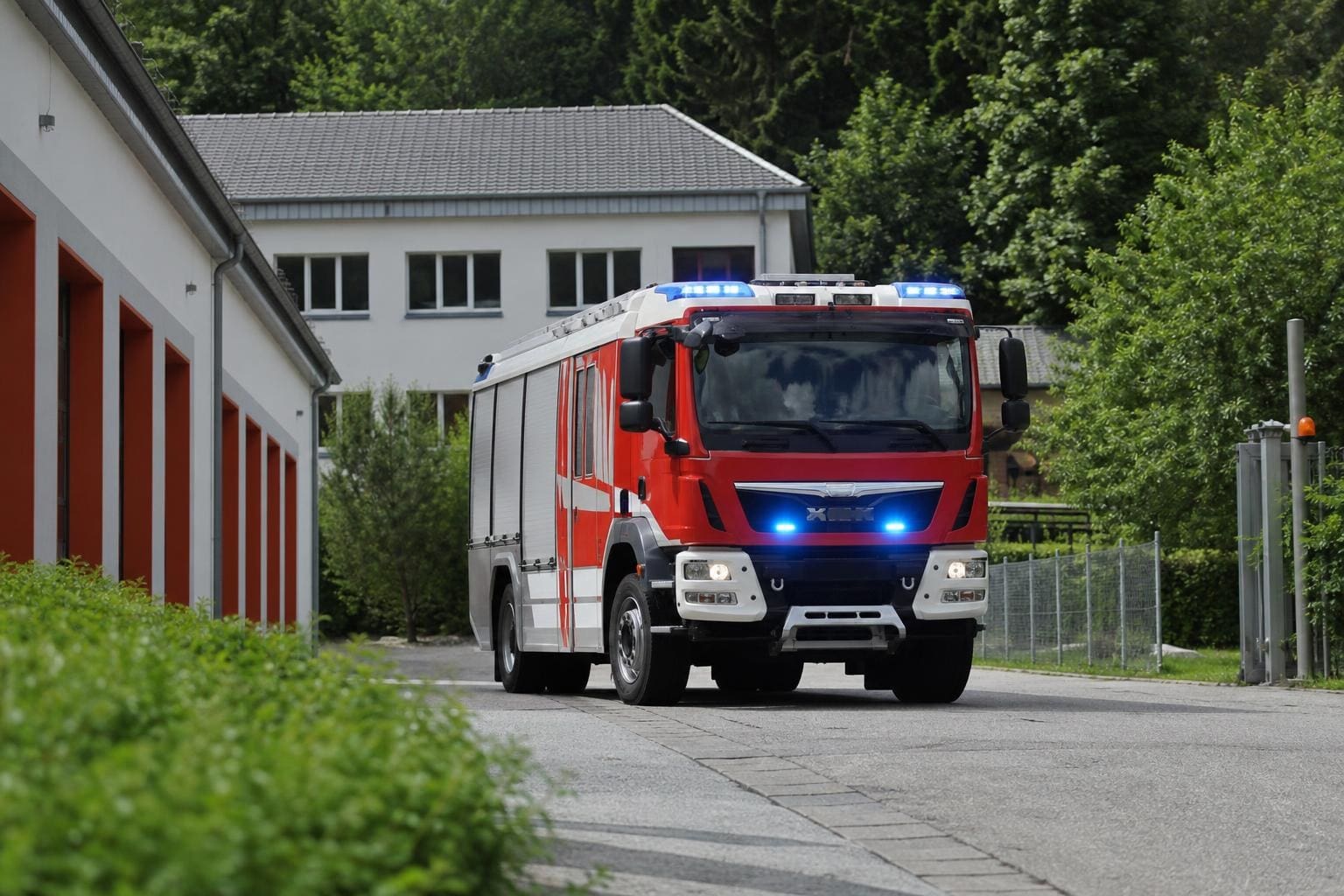 Rotes Feuerwehrfahrzeug mit leuchtenden blauen Blaulichtern vor einem weißen Gebäude