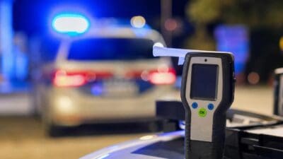 Ein Alkoholtester mit Mundstück vor einem unscharfen Polizeifahrzeug mit Blaulicht bei Nacht