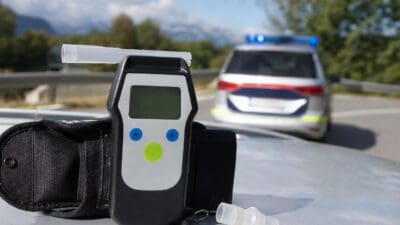Ein Alkoholtestgerät mit Mundstück liegt vor einem Polizeifahrzeug mit Blaulicht