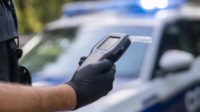 Polizist hält ein Alkoholmessgerät in der Hand vor einem Polizeiwagen mit Blaulicht