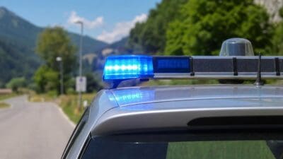 Blaues Blaulicht leuchtet auf dem Dach eines Polizeifahrzeugs vor einer Berglandschaft.