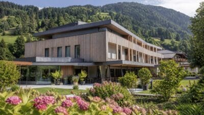 Modernes mehrstöckiges Gebäude des Altenwohnheims Kitzbühel vor bewaldeten Bergen und blühenden Sträuchern