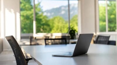 Ein Laptop steht auf einem Konferenztisch in einem modernen Büro mit großen Fenstern und Bergblick.