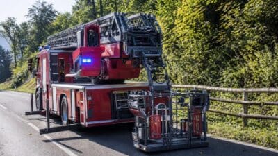 Rotes Feuerwehrfahrzeug mit ausgefahrener Drehleiter und Korb steht auf einer Straße