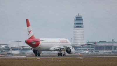 Weißes Flugzeug der Austrian Airlines mit rotem Heck auf einer Rollbahn vor einem Flughafentower