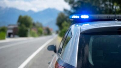 Polizeifahrzeug mit leuchtendem Blaulicht auf einer Landstraße mit Bergpanorama im Hintergrund