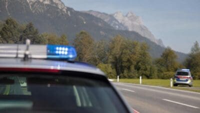 Polizeifahrzeug mit blauem Blaulicht im Vordergrund und weiteres Einsatzfahrzeug auf der Straße vor Bergen