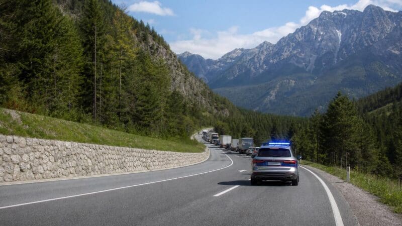 Polizeifahrzeug mit Blaulicht auf einer kurvigen Bergstraße vor einer Verkehrskolonne
