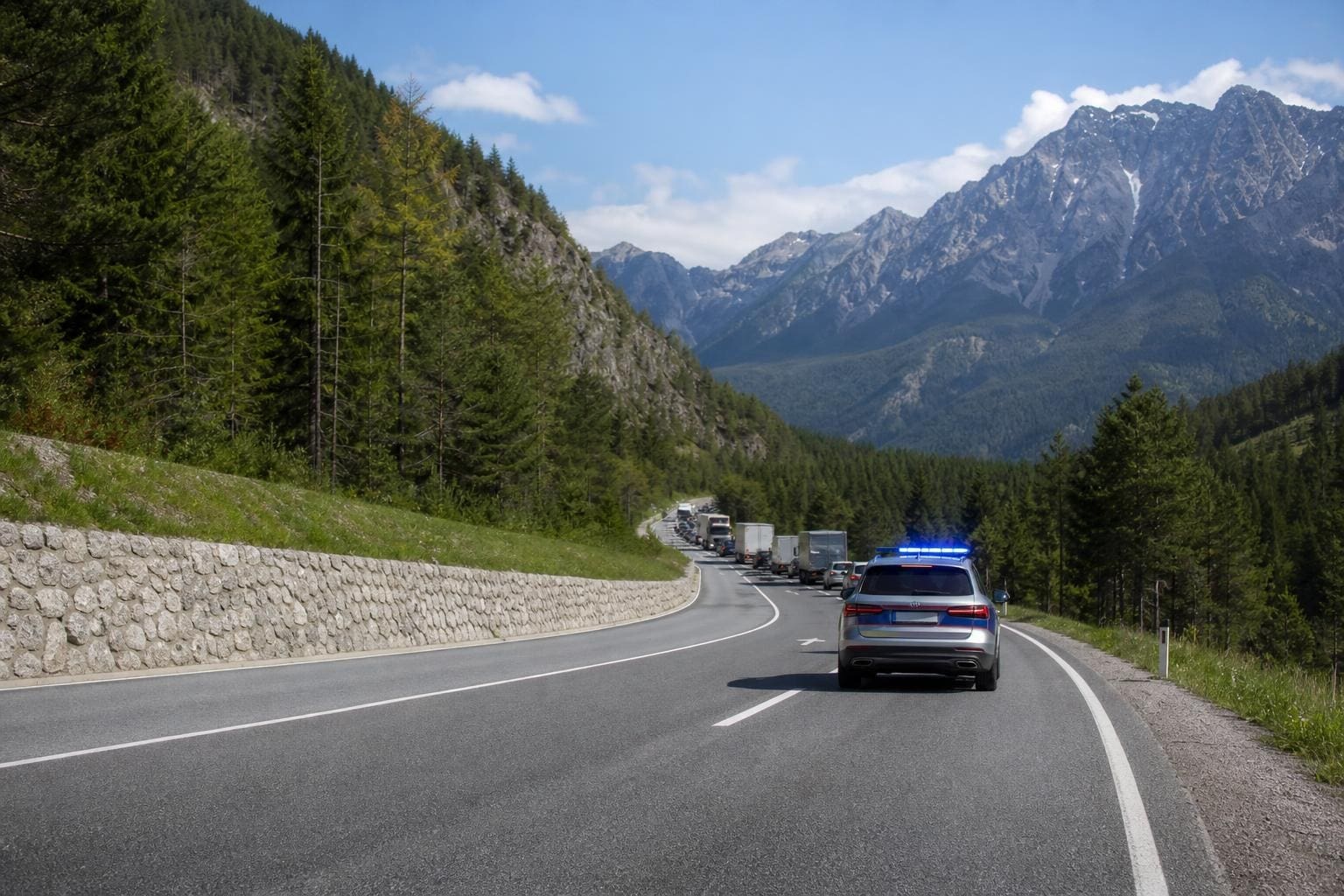 Polizeifahrzeug mit Blaulicht auf einer kurvigen Bergstraße vor einer Verkehrskolonne